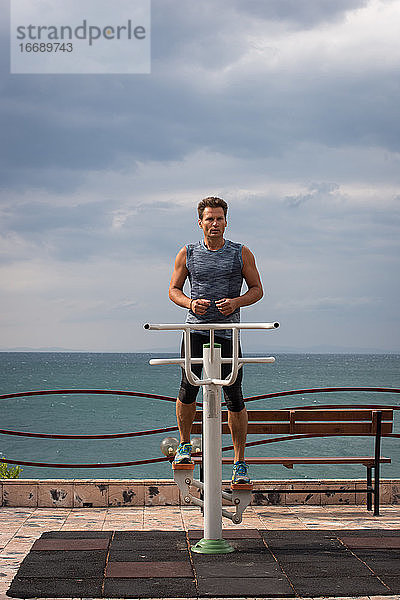 Erwachsener Mann trainiert am Morgen auf Sportgeräten am Meer