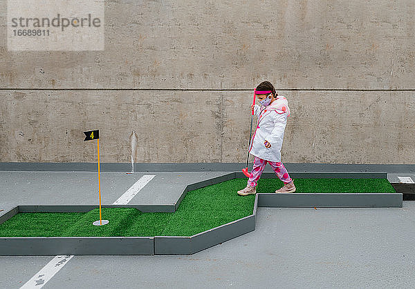 Mädchen im Arztkostüm spielt Minigolf auf einem Parkplatz