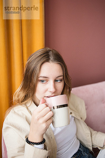 Junge Frau in Großaufnahme trinkt Tee  Kaffee in einer Keramiktasse im Wohnzimmer