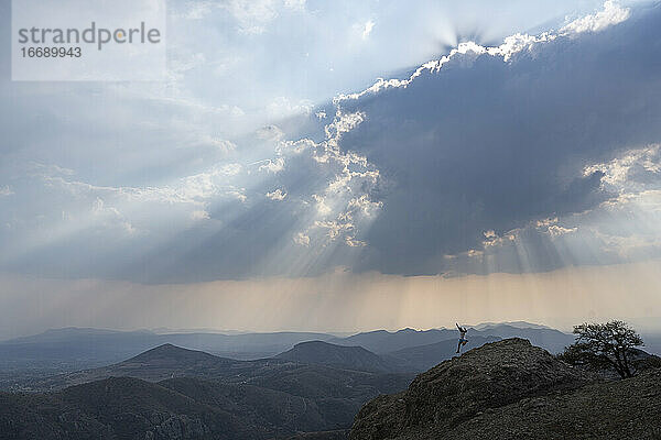 Ein Mann läuft bergab auf einem Felsen unter einem bewölkten Himmel mit Sonnenstrahlen