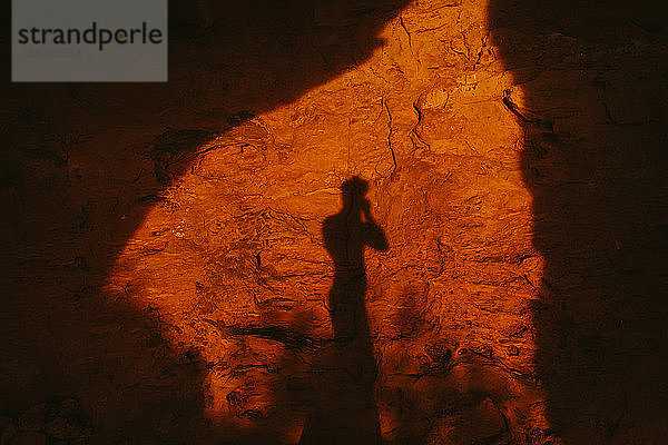 Silhouette einer Person gegen roten Höhleneingang bei Sonnenuntergang in der Wüste