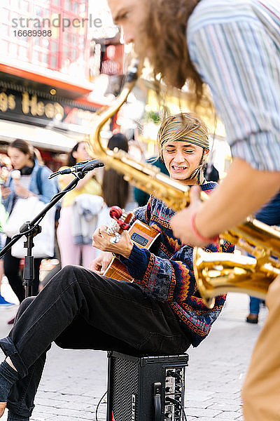 Selektiver Fokus auf das Gesicht eines singenden Mannes  der neben einem Saxophonisten auf der Straße Gitarre spielt
