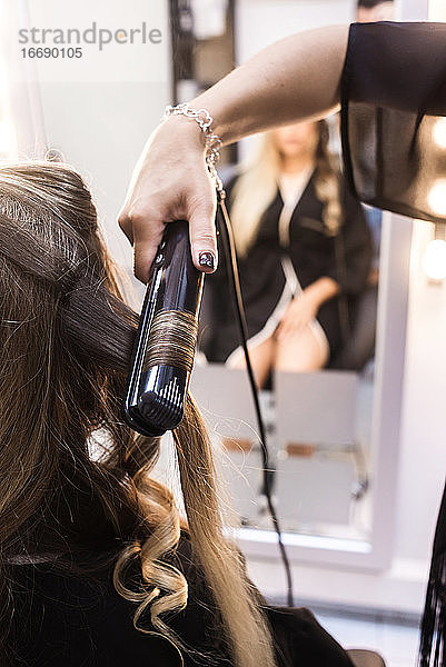 Nahaufnahme eines Friseurs  der einer Kundin im Friseursalon die Haare lockt