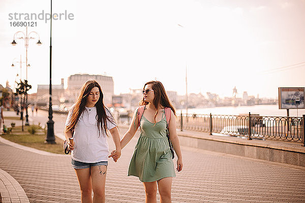 Lesbisches Paar  das sich im Sommer beim Spazierengehen in der Stadt unterhält und die Hände hält