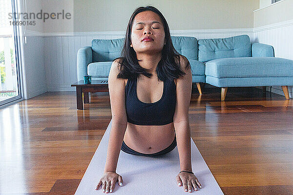 Junge Frau macht Yoga auf Yogamatte zu Hause