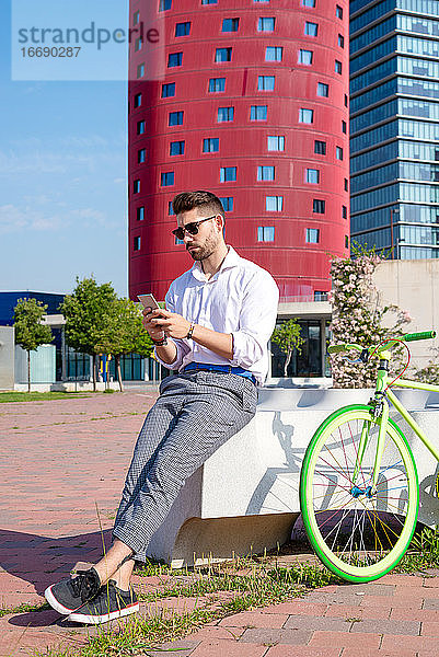 Outdoor-Porträt eines gut aussehenden jungen Mannes mit Mobiltelefon und Fahrrad mit festem Gang auf der Straße.