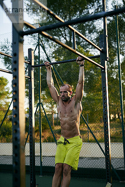 Shirtless fit junger Mann trainiert in einem Käfig im Freien Fitnessstudio
