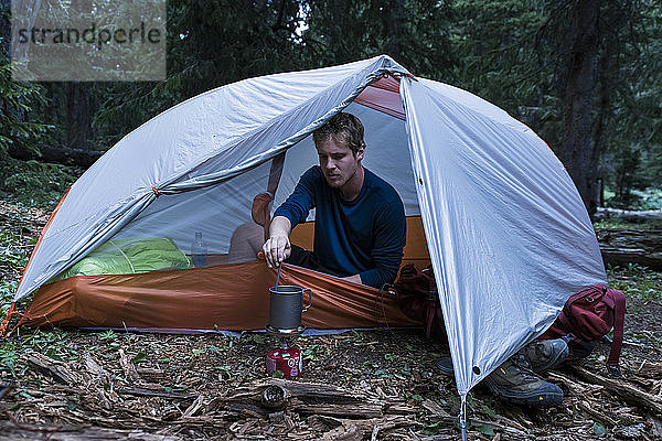 Männlicher Wanderer bei der Essenszubereitung beim Zelten im Wald