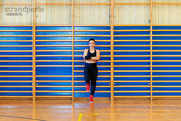 Weibliche Kämpferin lehnt sich im Fitnessstudio an eine Leiter aus Holzstäben und schaut in die Kamera