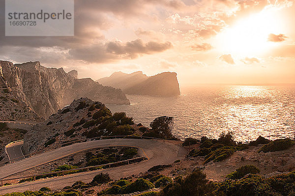 Kurvenreiche Straße und Steilküste auf Mallorca mit rötlichen Tönen des Sonnenuntergangs