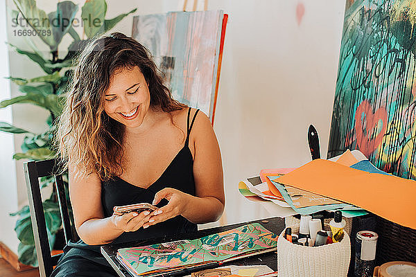 Eine Malerin benutzt ihr Smartphone  während sie im Atelier an ihren Bildern arbeitet