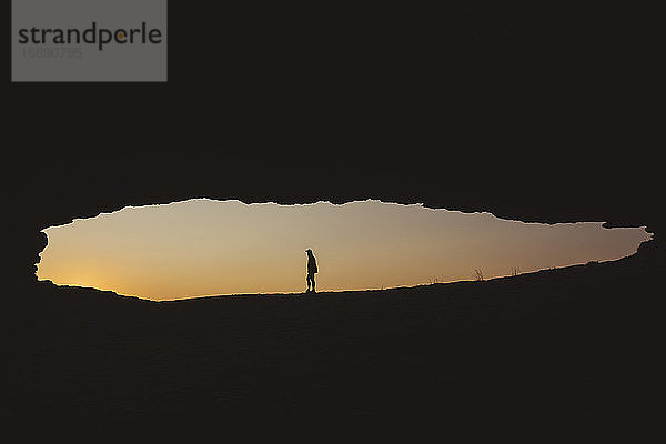 Ein Mann steht vor einer Felsenhöhle am Meer und beobachtet den Sonnenaufgang  Kantabrien  Spanien