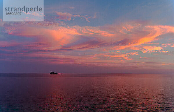 Sonnenuntergang in Benidorm / Valencia / Spanien mit einem bewölkten blauen und orangenen Himmel und einer Insel am Horizont des Mittelmeers mit einer orangen  roten  blauen und rosa Farbe. Horizontal Foto