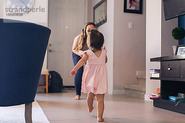 Baby-Mädchen in rosa Kleid zu Fuß in Richtung Mama zu Hause.
