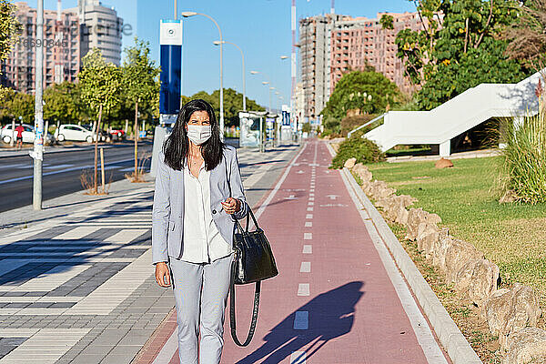 Frau geht mit einer Maske die Straße entlang.