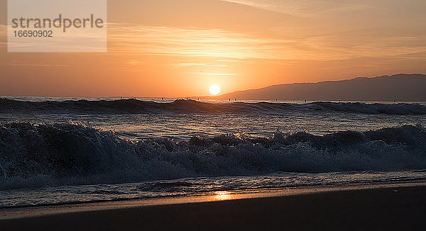 Kalifornischer Sonnenuntergang über den Wellen des Pazifiks mit Malibu in der Ferne