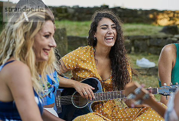 Lächelnde Frau spielt Gitarre und hat Spaß mit einer Gruppe von Freunden
