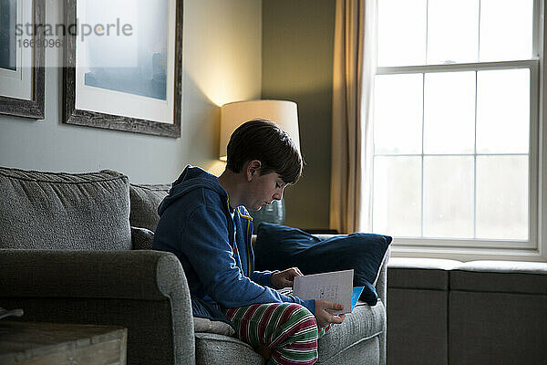 Close Up Seitenansicht von Teen Boy sitzt auf Couch Lesen Geburtstagskarte