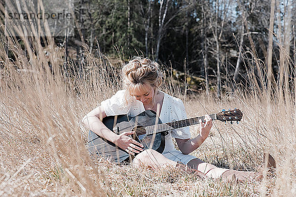 Frau saß auf einem Feld und spielte fröhlich Gitarre im Sommer