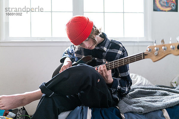 Musiker sitzt auf der Bettkante und spielt Gitarre in einem hellen  sonnigen Raum