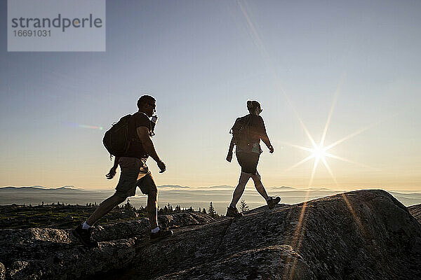 Zwei Wanderer erreichen bei Sonnenaufgang den Gipfel eines Berges in Maine