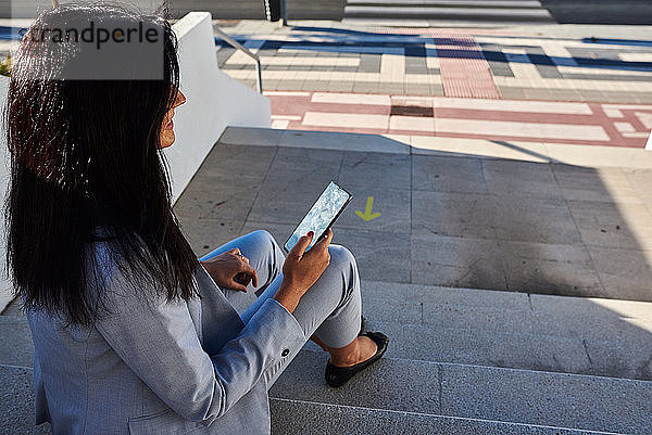 Geschäftsfrau auf einer Treppe sitzend mit Smartphone in der Hand.