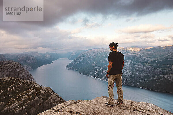 Mann steht und schaut auf den Rand einer Klippe am Preikestolen  Norwegen  hinunter