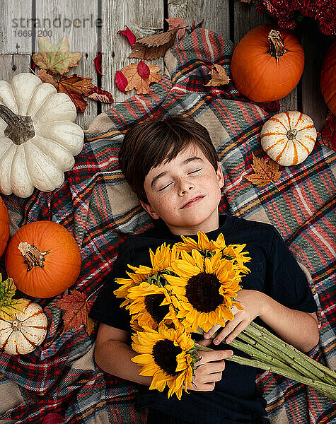 Draufsicht auf einen Jungen  der Sonnenblumen hält  umgeben von Herbstartikeln.