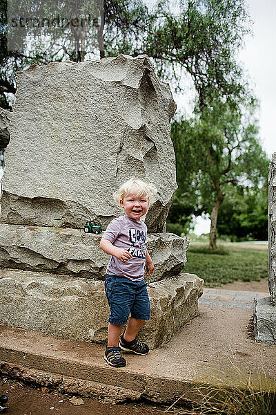 Zweijähriges Kind lächelt und steht neben einem Felsen
