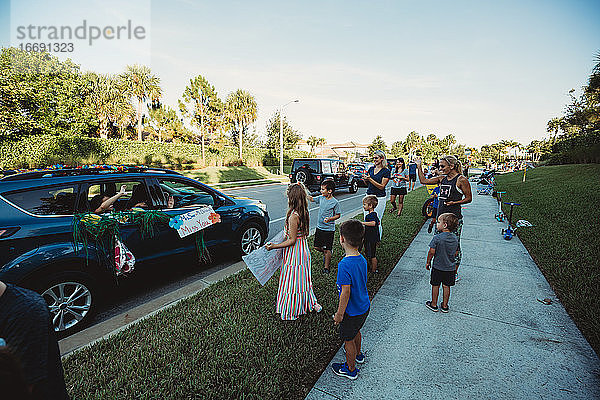 Kinder winken den Lehrern bei der Autoparade in der Nachbarschaft zu