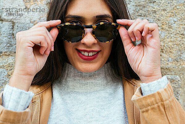 Schöne junge Frau posiert über einer Mauer mit Sonnenbrille
