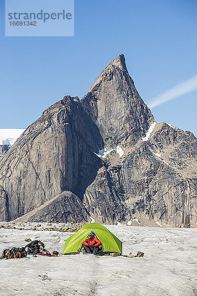 Bergsteiger sitzt im Zelt unter einem großen  schönen Berggipfel.