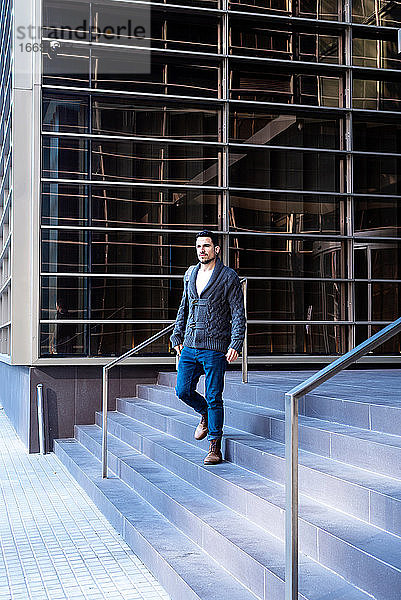 Junger bärtiger Mann geht die Treppe eines Bürogebäudes hinunter