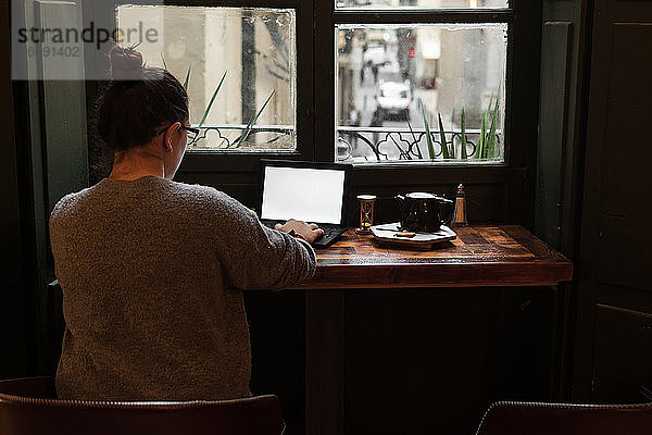 Ein junger Student arbeitet an einem Tisch in der Nähe eines Kneipenfensters