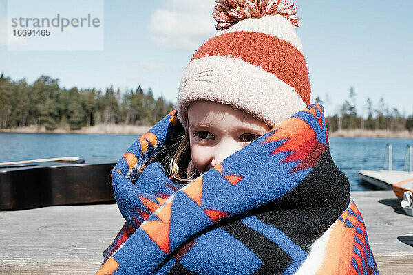 ein junges Mädchen  das sich in eine Decke eingewickelt am See wärmt