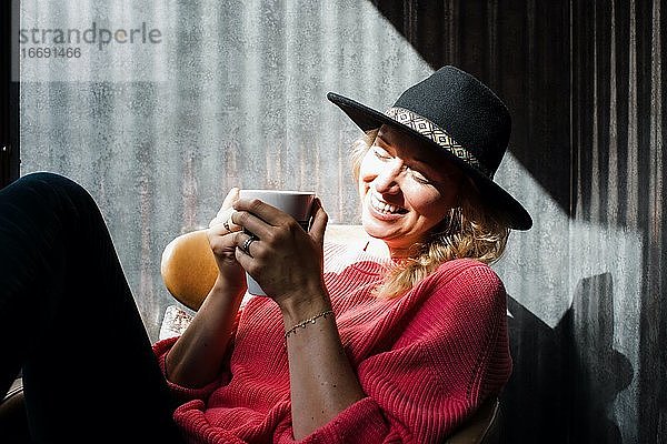 Porträt einer Frau  die in einem Café Kaffee trinkt und in die Sonne lächelt