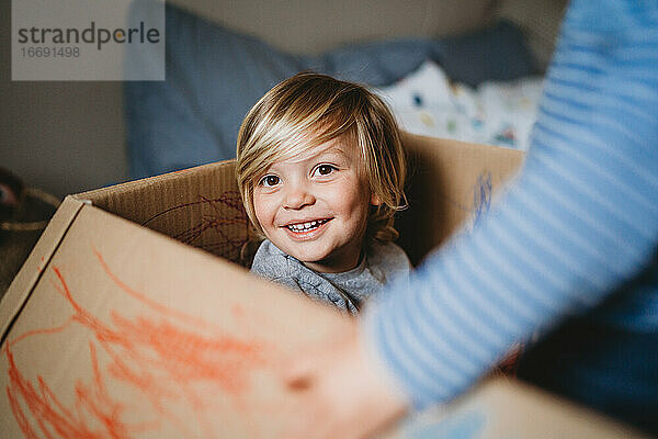 Junges männliches Kind  das lächelnd in die Kamera schaut und in einer Schachtel spielt