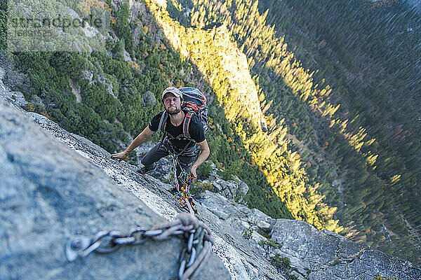 Mann schaut nach oben und macht ein lustiges Gesicht  während er sich am El Capitan abseilt