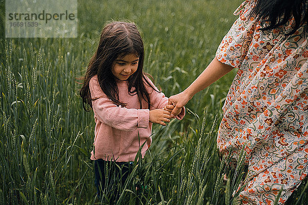 Lächelndes Mädchen  das die Hand seiner Mutter hält  während es im Feld spazieren geht