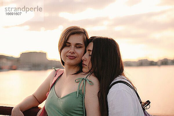 Porträt eines glücklichen lesbischen Paares  das bei Sonnenuntergang auf einer Brücke steht