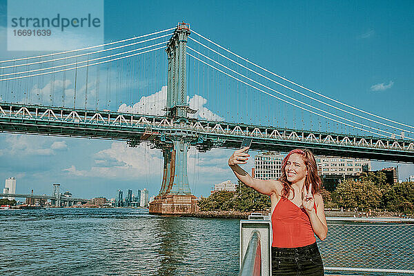 Junge Frau steht am Fluss und macht ein Selfie.