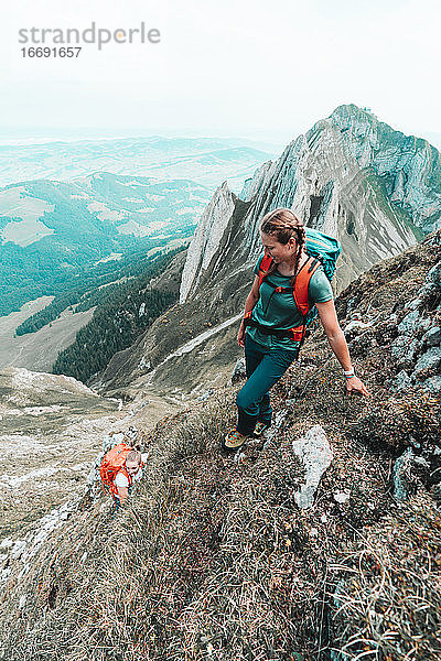 Zwei aktive Bergsteigerinnen beim Aufstieg auf einen steilen Grasberg in der CH