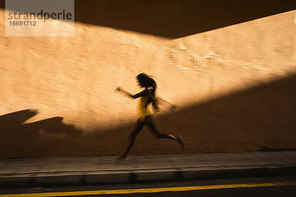 Künstlerische Geschwindigkeitsunschärfe einer jungen Frau  die gegen eine gelbe Wand läuft