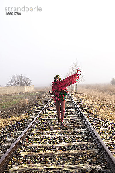 Vorderansicht einer Frau mit Kopftuch  die auf einer Eisenbahnstrecke geht