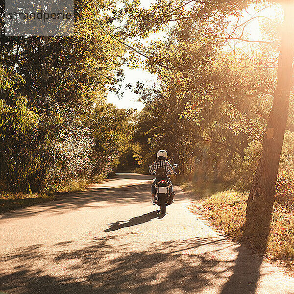 Rückansicht einer Motorrad fahrenden Frau auf einer Landstraße im Wald