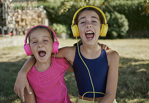 Kleine Mädchen hören Musik und lächeln mit gelben und rosa Kopfhörer in einem Garten. Glück Konzept