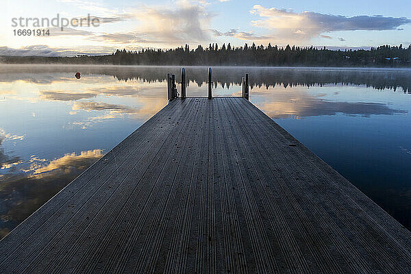 Holzsteg mit Leiter am See bei Sonnenuntergang und Spiegelung der Wolken