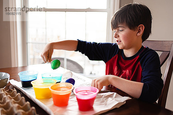 Ein Junge taucht ein Ei in eine Schale mit Farbstoff  um es für Ostern zu färben.