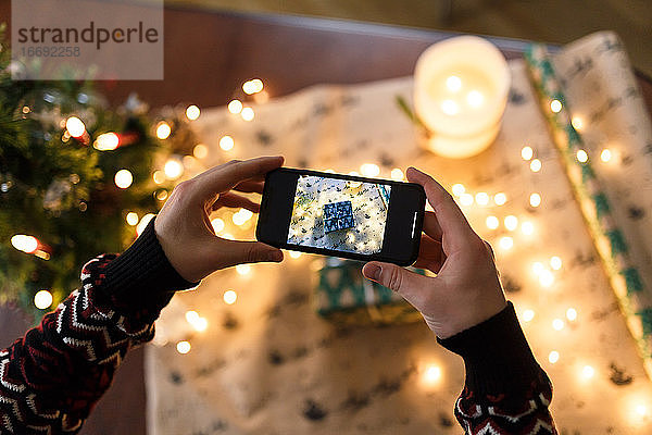 Mann fotografiert mit Smartphone sorgfältig verpacktes Weihnachtsgeschenk