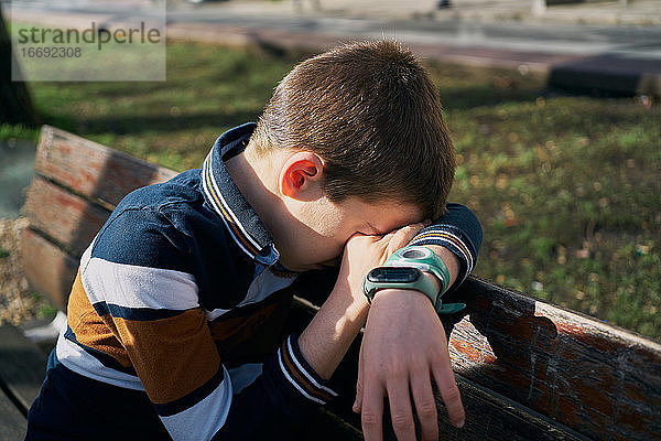 Kind auf einer Bank bedeckt sein Gesicht mit seinem Arm und weint